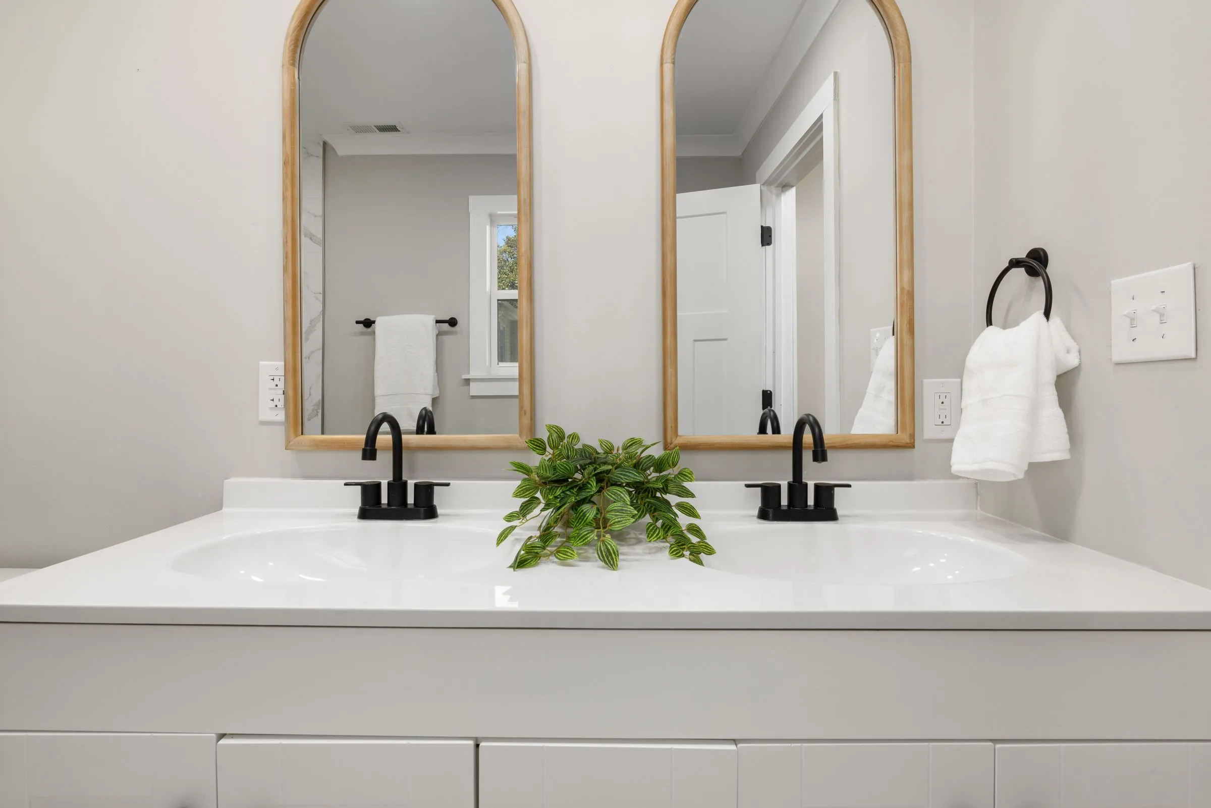 Double vanity with two brass-framed arched mirrors, black faucets and a white counter